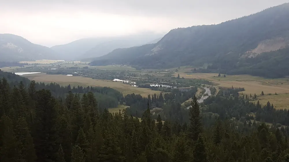 Sweeping aerial view of a misty Colorado mountain valley with evergreen forests and a winding river representing City to Summit Courier's commitment to mountain communities